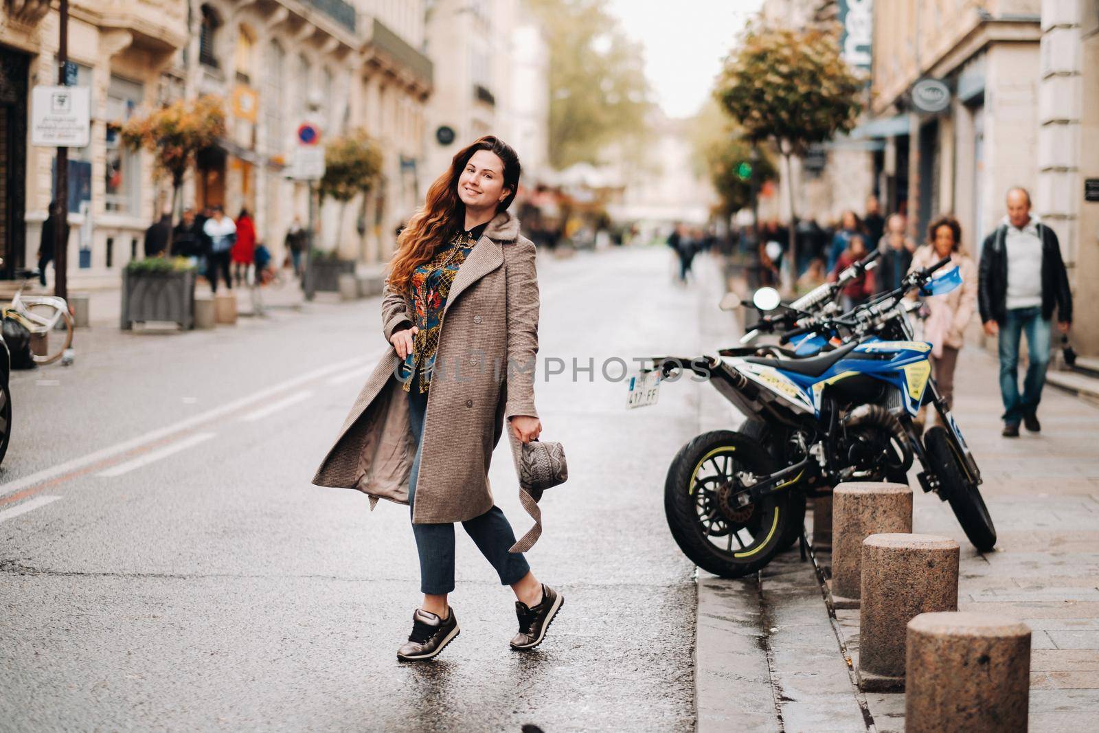 a beautiful romantic girl in a coat with her hair down runs through the old city of Avignon. France. Girl in a coat in France.