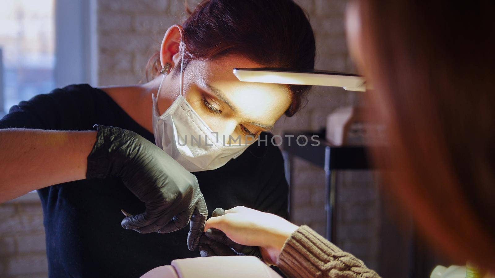 Working manicurist - nail master in medical mask doing professional manicure, telephoto