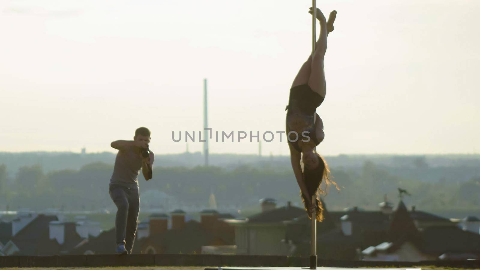 Sport sexy attractive girl posing on pole on nature for two photographer over the skyline, telephoto