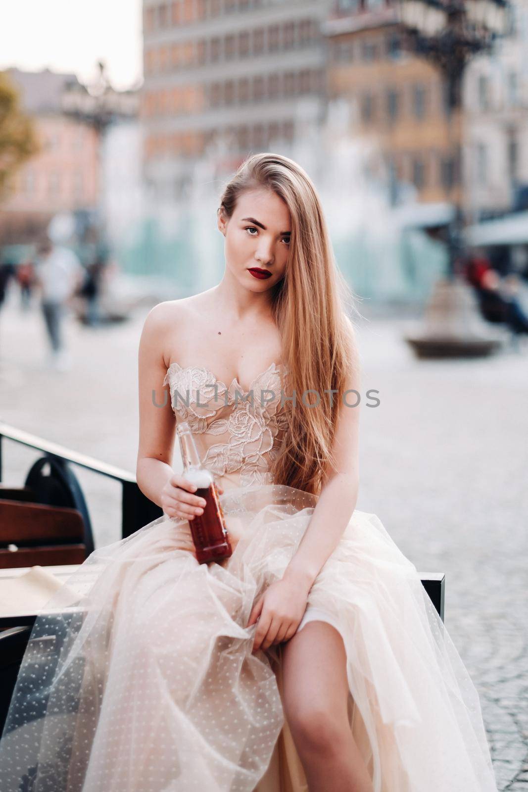 A bride in a wedding dress with long hair and a drink bottle in the Old town of Wroclaw. Wedding photo shoot in the center of an old Polish city.Wroclaw, Poland.