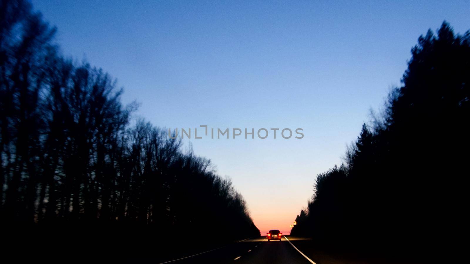 Cars moving on forest road against sunrise, horizontal