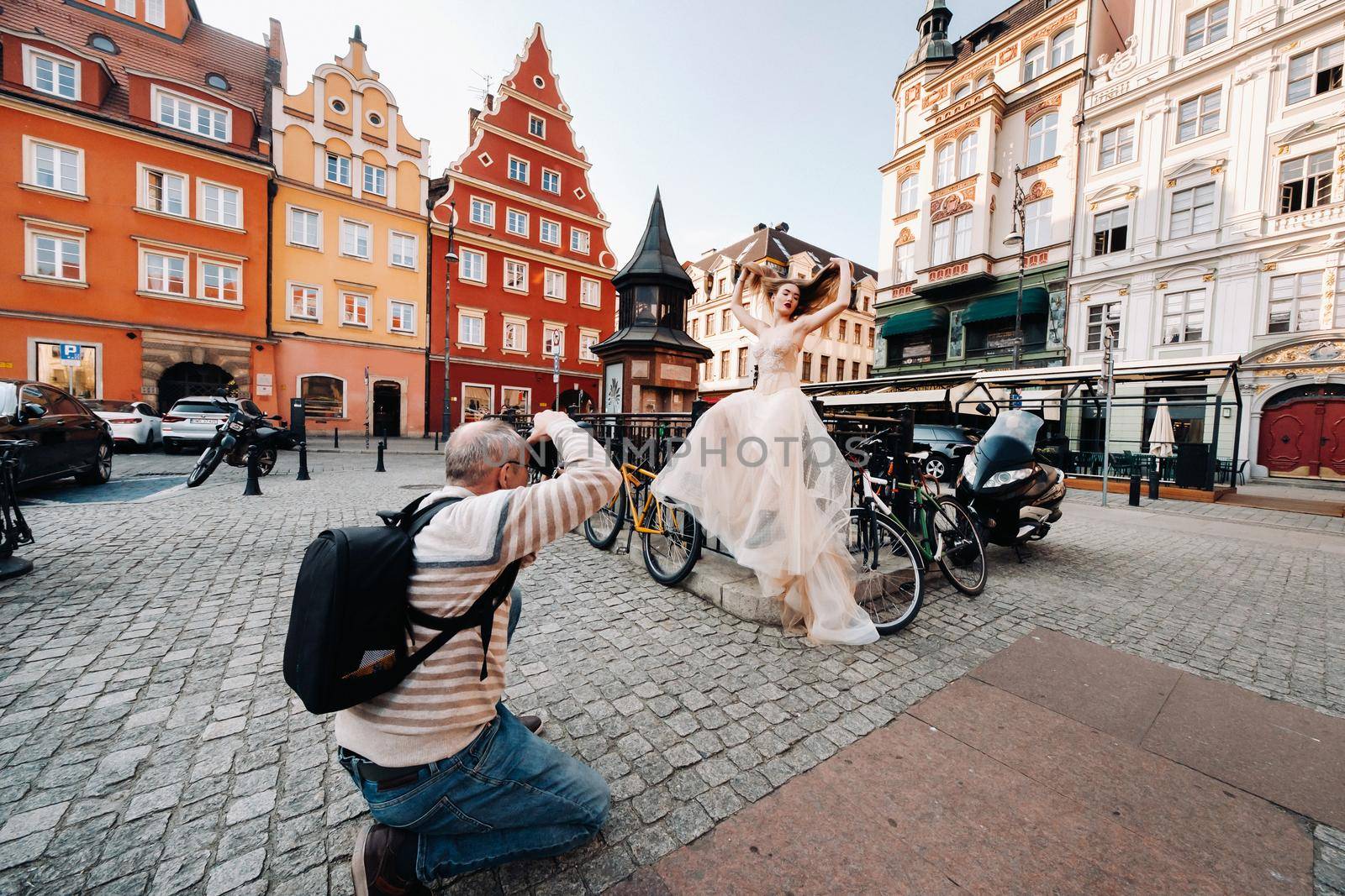 a photographer photographs a Bride in a wedding dress with long hair in the Old town of Wroclaw. Wedding photo shoot in the center of an old Polish city.Wroclaw, Poland.