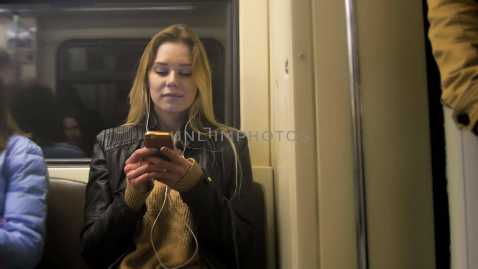 happy girl with long blonde hair in leather jacket with straightens hair use gadget in metro, close up
