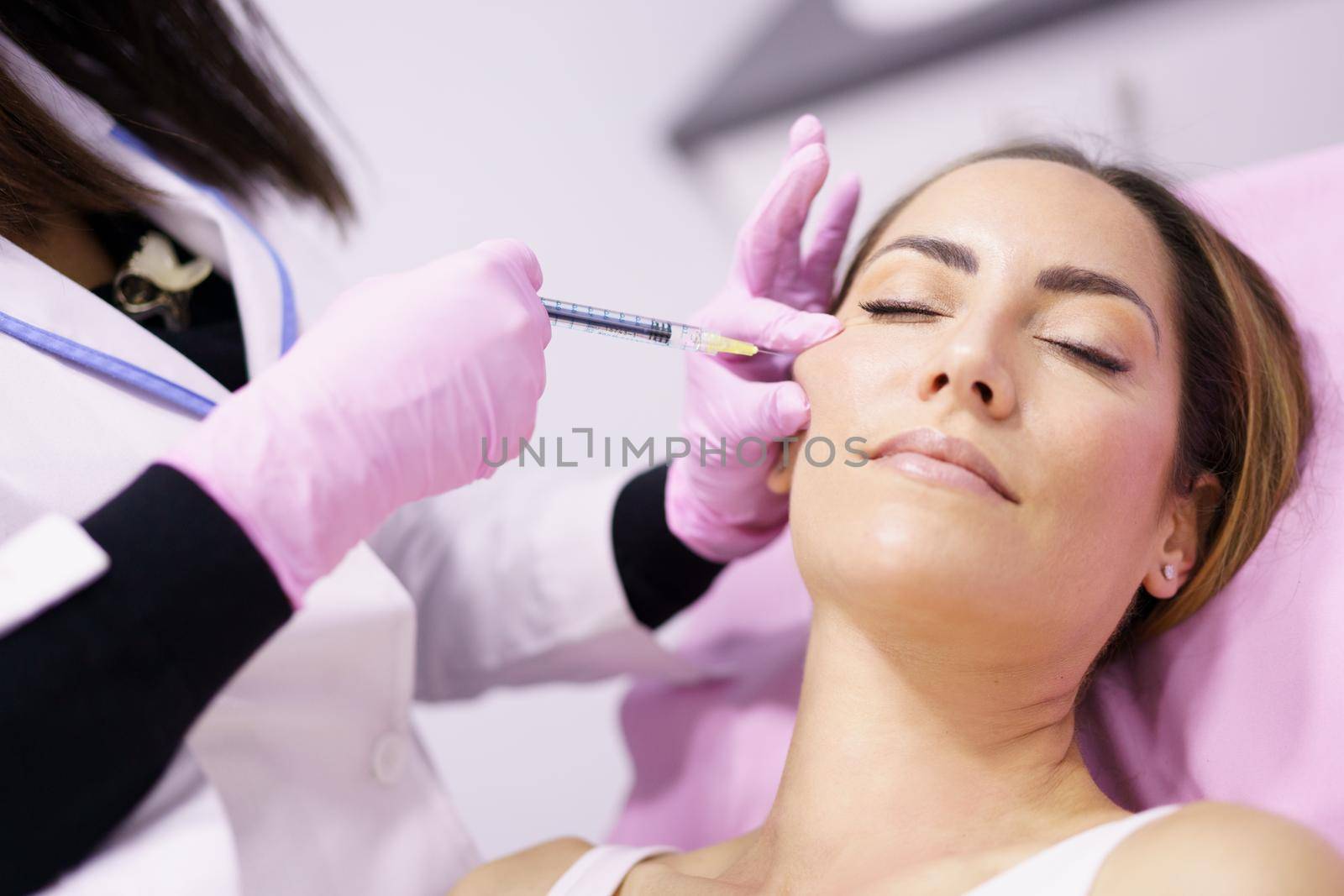 Doctor injecting hyaluronic acid into the cheekbones of a middle-aged woman as a facial rejuvenation treatment.