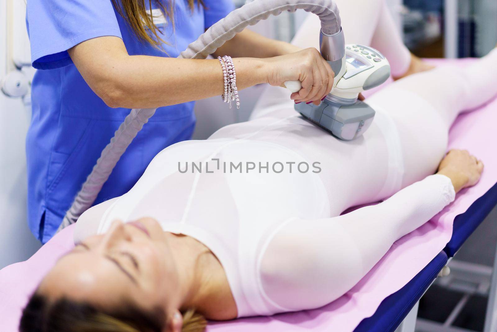 Middle-aged woman in special white suit having a anti cellulite belly massage with spa apparatus