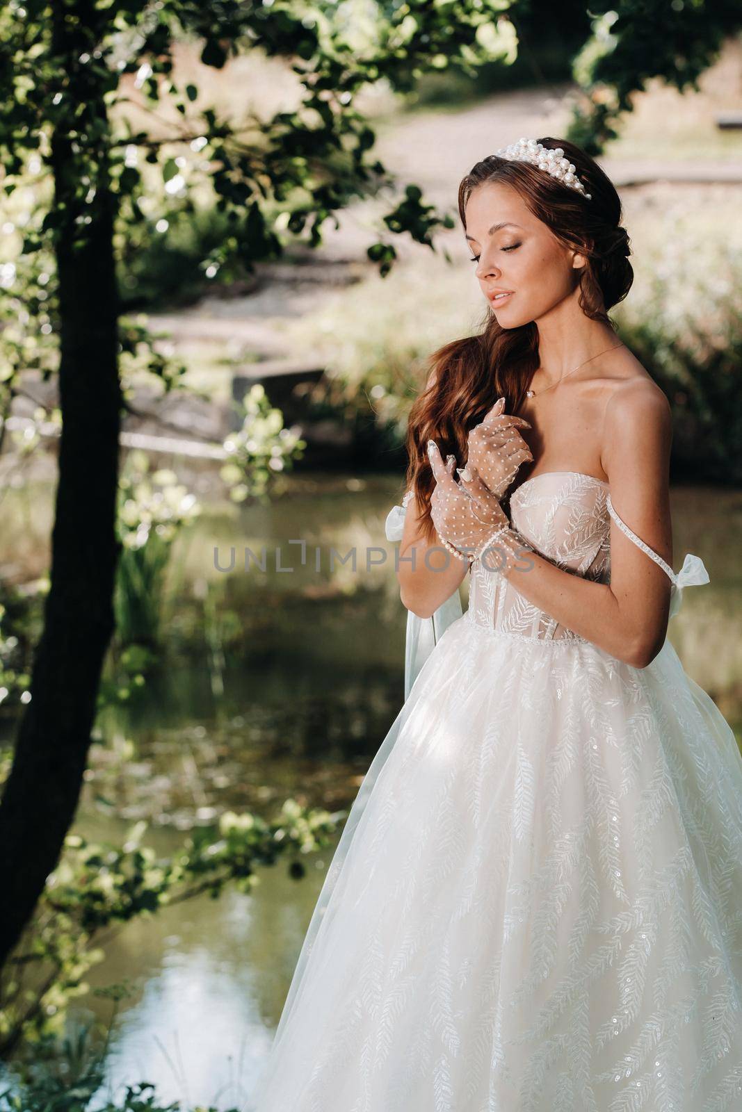 An elegant bride in a white dress, gloves with a bouquet on a waterfall in the Park, enjoying nature.Model in a wedding dress and gloves in the forest.Belarus by Lobachad