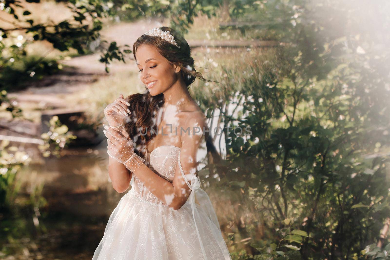 An elegant bride in a white dress, gloves with a bouquet on a waterfall in the Park, enjoying nature.Model in a wedding dress and gloves in the forest.Belarus by Lobachad