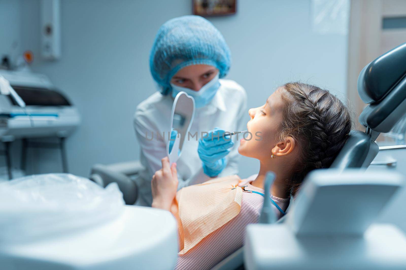 Little girl patient and dentist are checking teeth at mirror after dental treatment in dental office. Dentistry concept