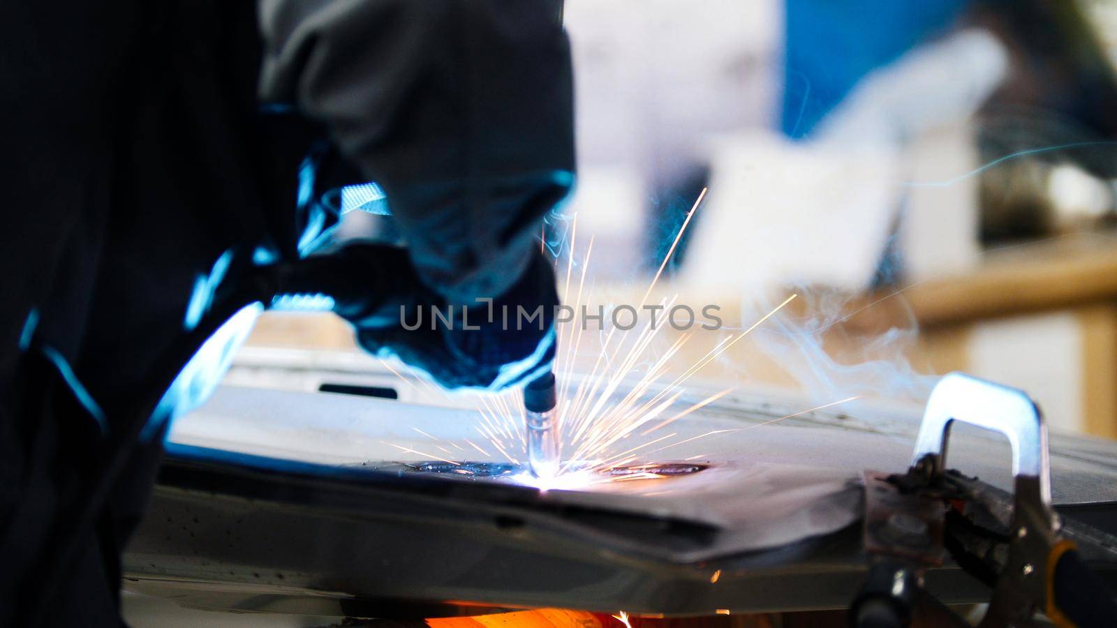 Welding industrial: worker in helmet repair detail in car service, telephoto