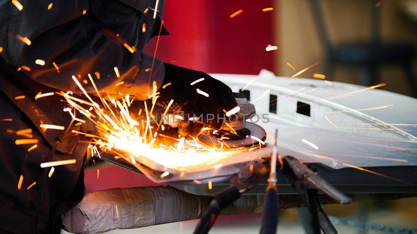 Professional car service - worker grinding metal construction with a circular saw, close up, telephoto