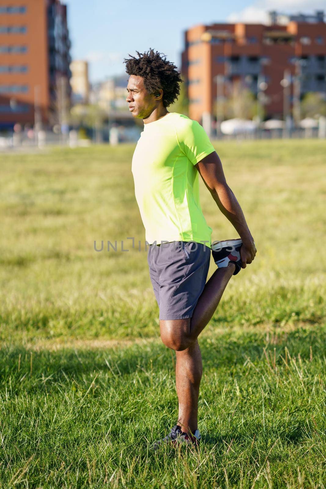 Black man stretching his quadriceps after running outdoors. Young male exercising in urban background.