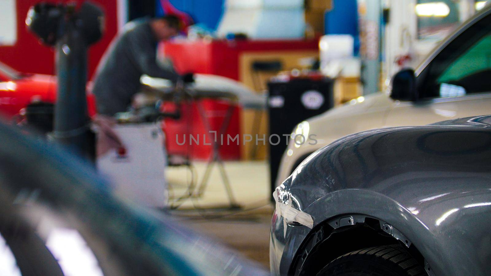 Mechanic in car service fixing and repairing detail of automobile, defocused background, wide angle