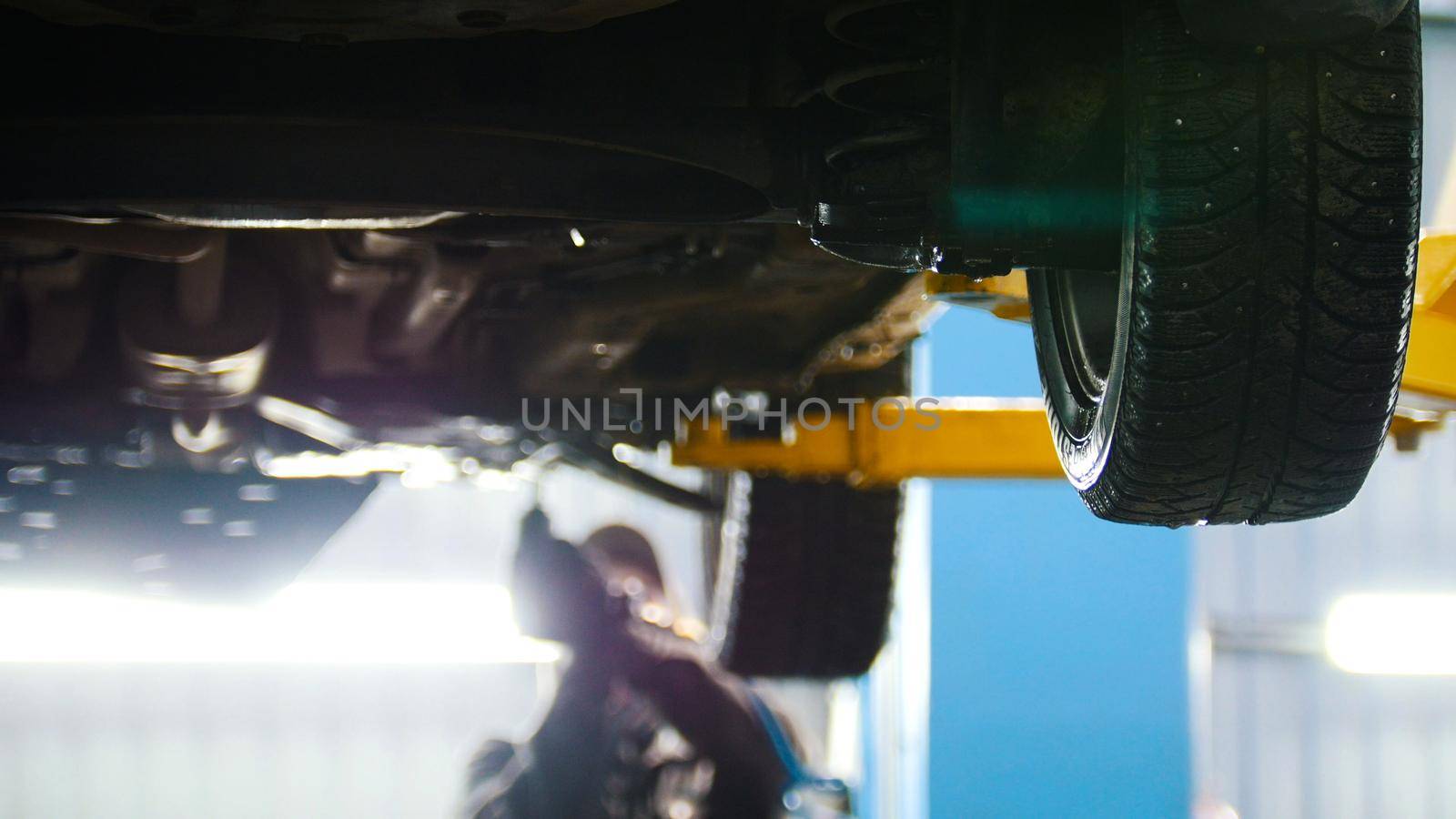 Automobile diagnostic - mechanic working under a lifted car, de-focused background, backlight