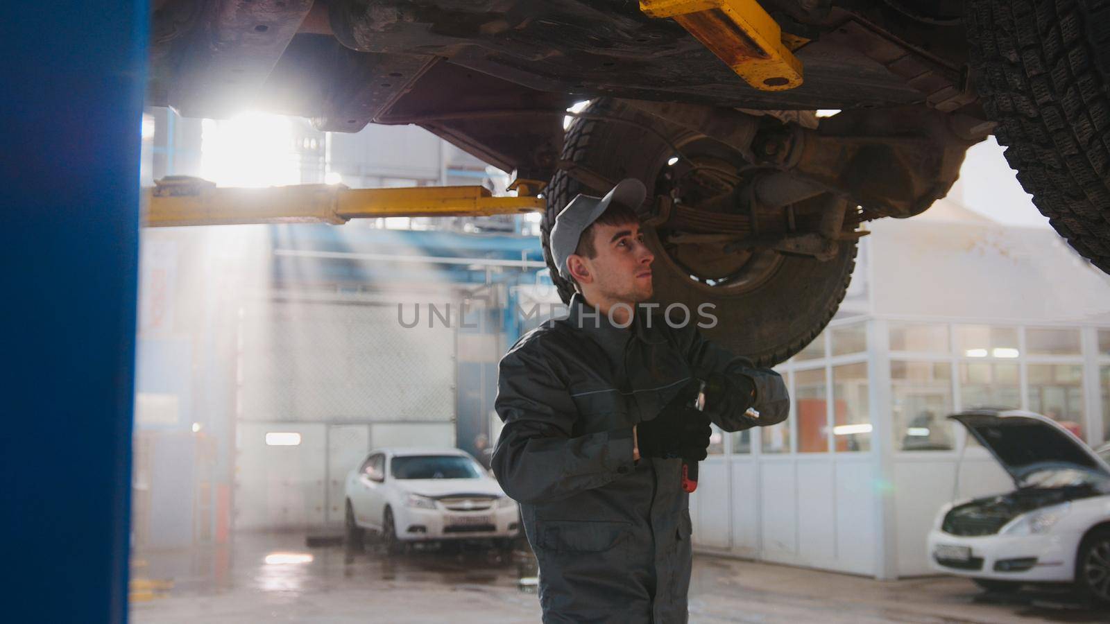 Garage automobile service - a mechanic under bottom of car checks the wheel, close up, horizontal