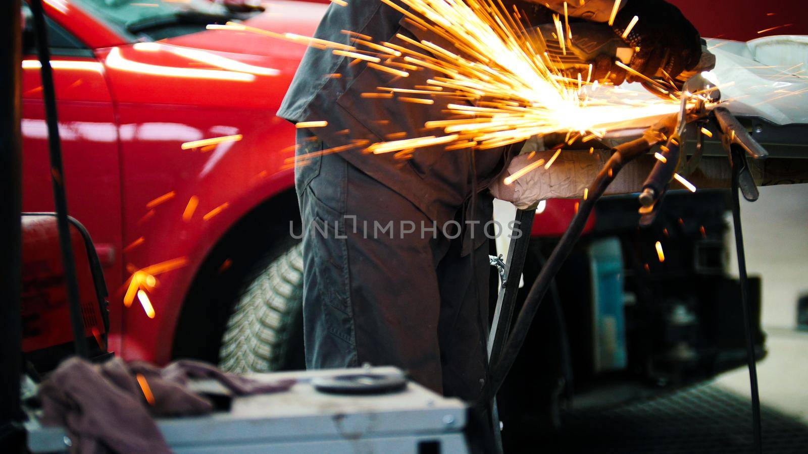 Car auto service - worker grinding metal construction with a circular saw, telephoto