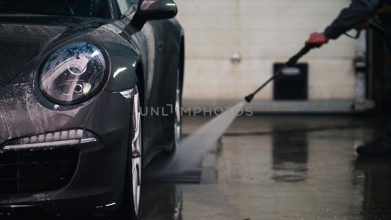 Worker in auto service is washing a luxury car in the suds by water hoses by Studia72