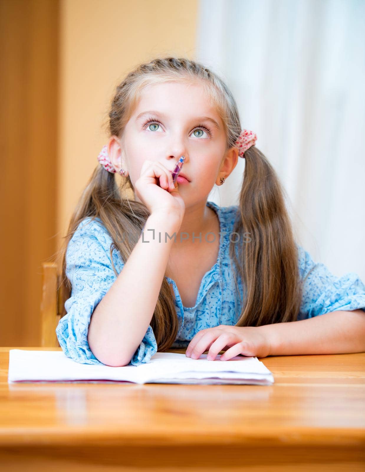 Cute pensive little girl studying at home and smiling