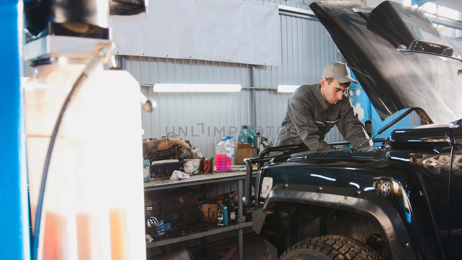 Mechanic in automobile garage checking hood of the car, wide angle, horizontal