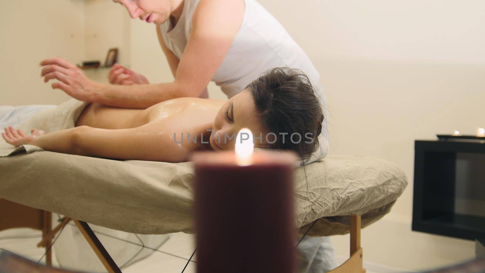 Massage parlor - man doing relaxing therapy for a young girl, candle in room, close up
