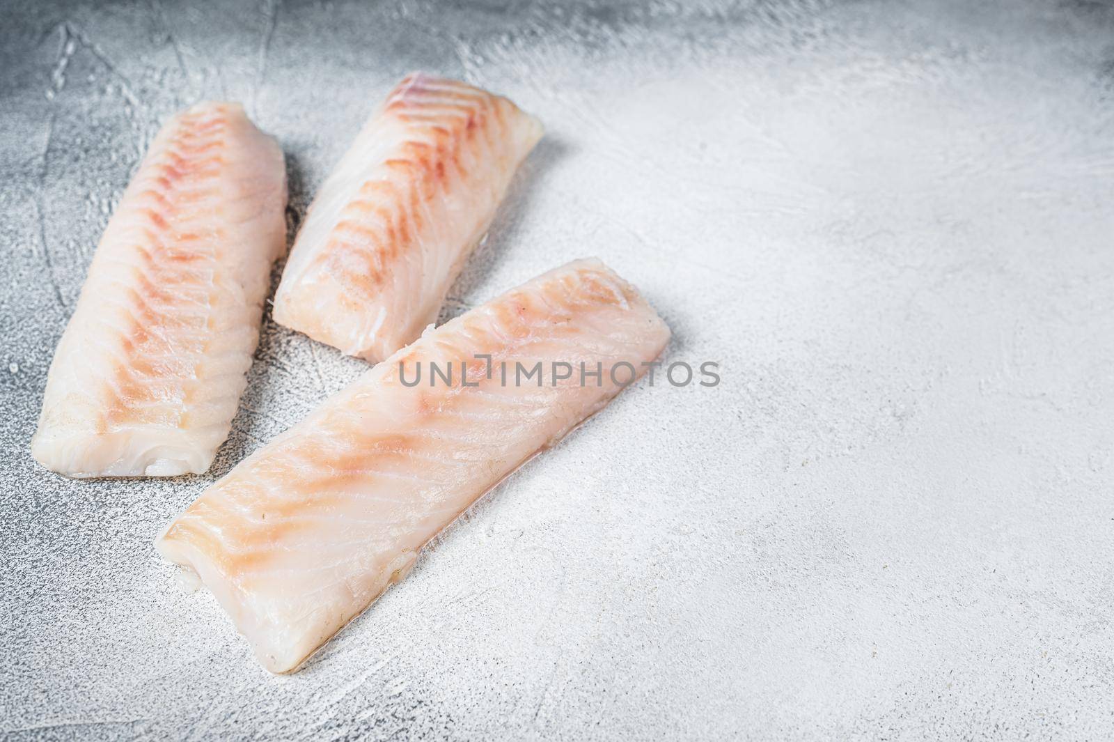 Raw Norwegian cod fish fillet on kitchen table. White background. Top view. Copy space by Composter