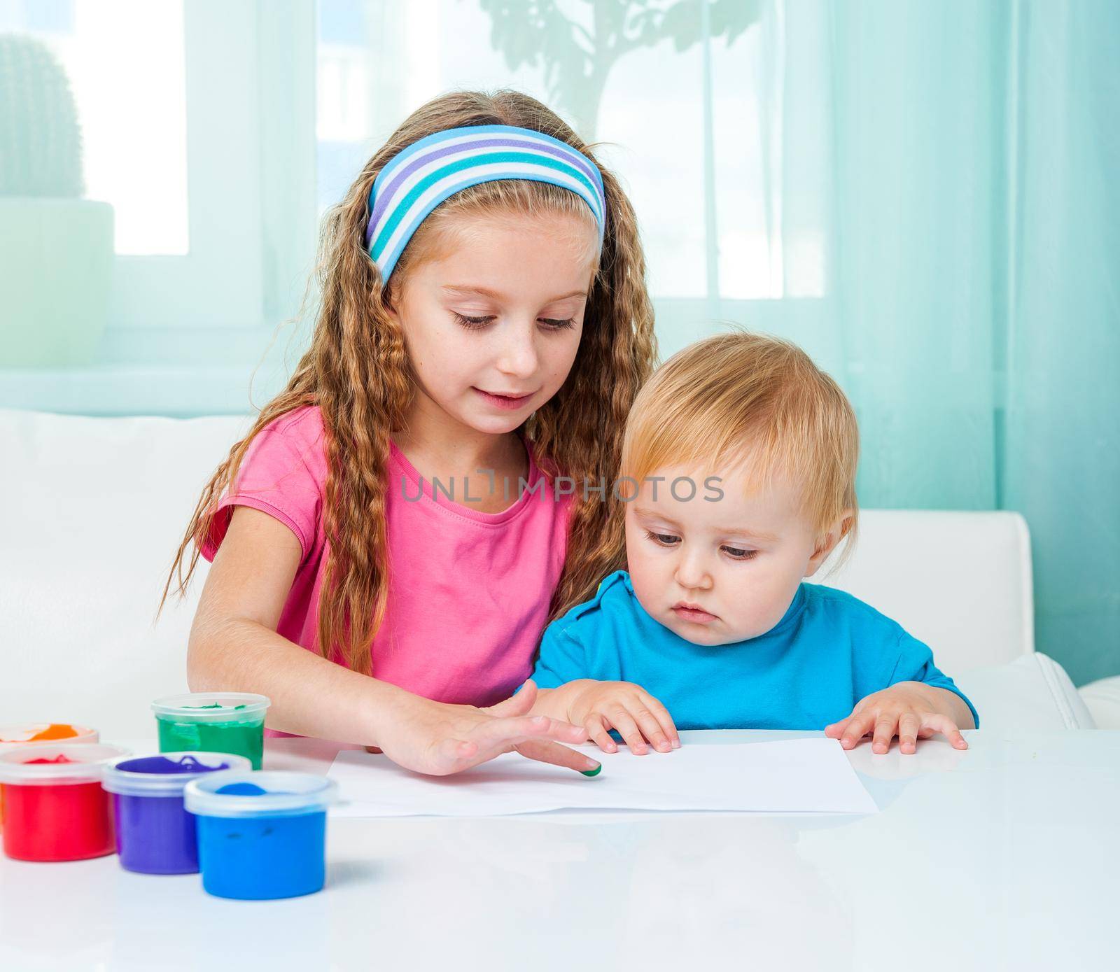 two cute sisters draw finger paints at home in bright living room