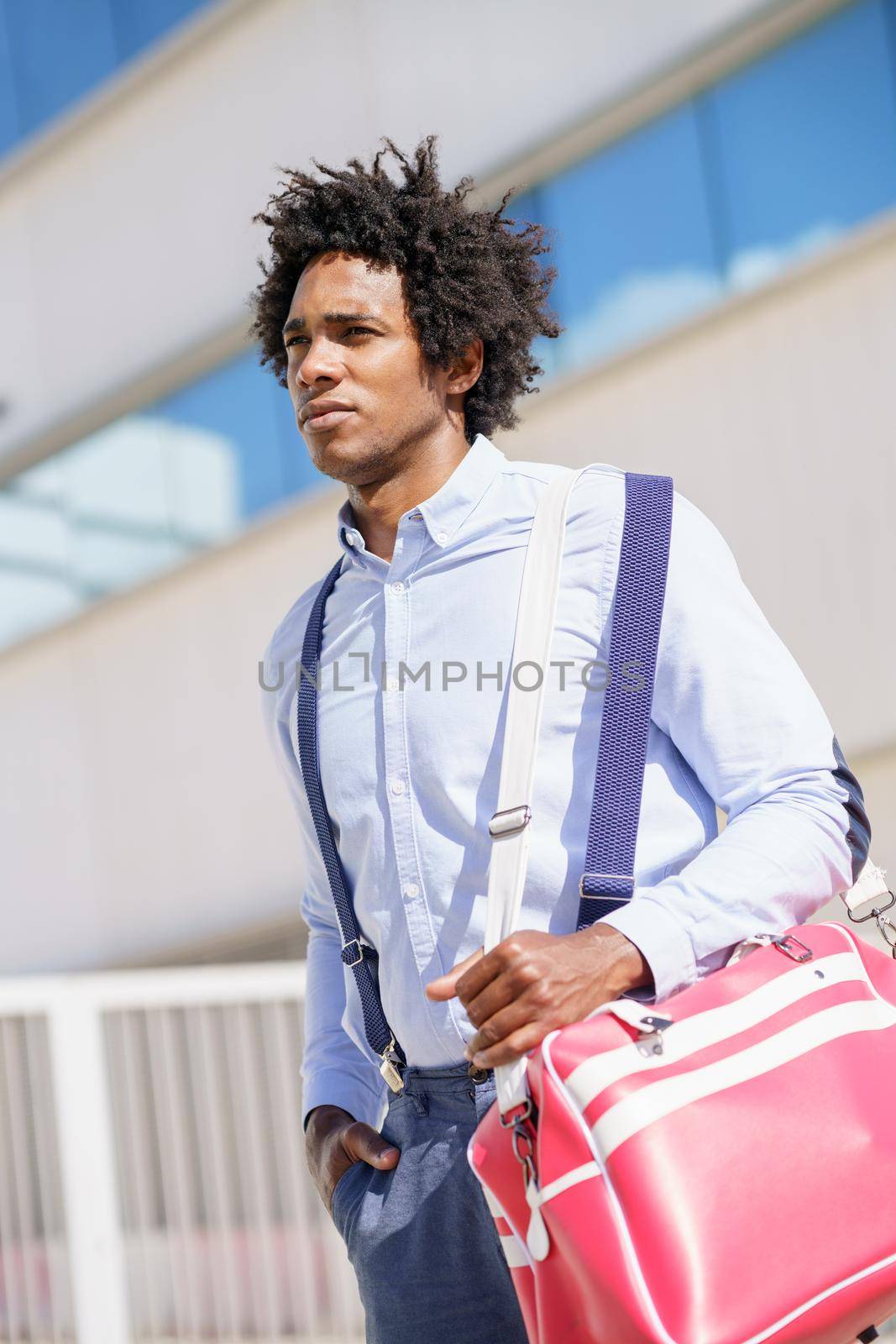 Black businessman with afro hair walking near an office building with a sports bag.