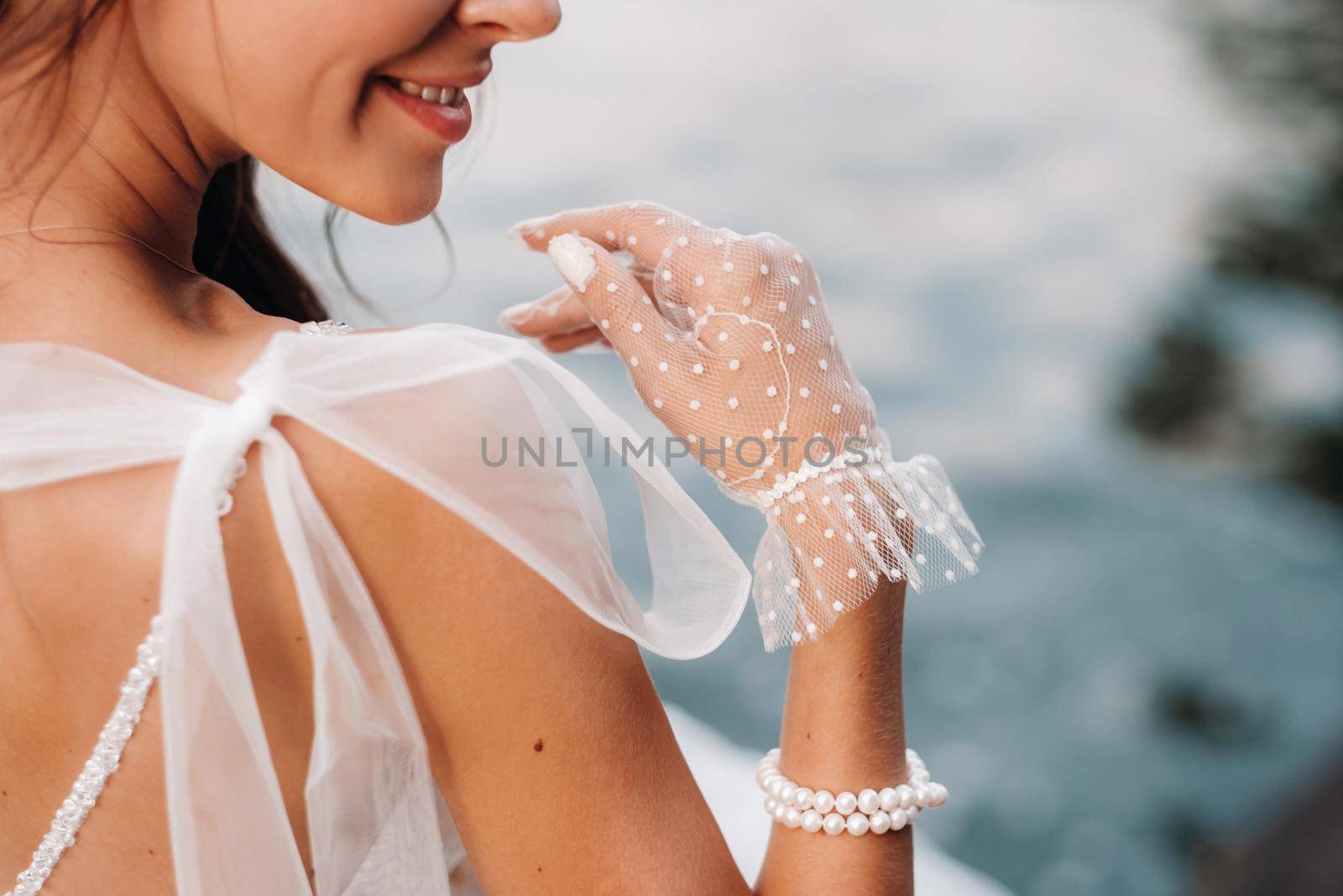 An elegant bride in a white dress and gloves is sitting by the lake in the Park, enjoying nature.A model in a wedding dress and gloves in a nature Park.Belarus