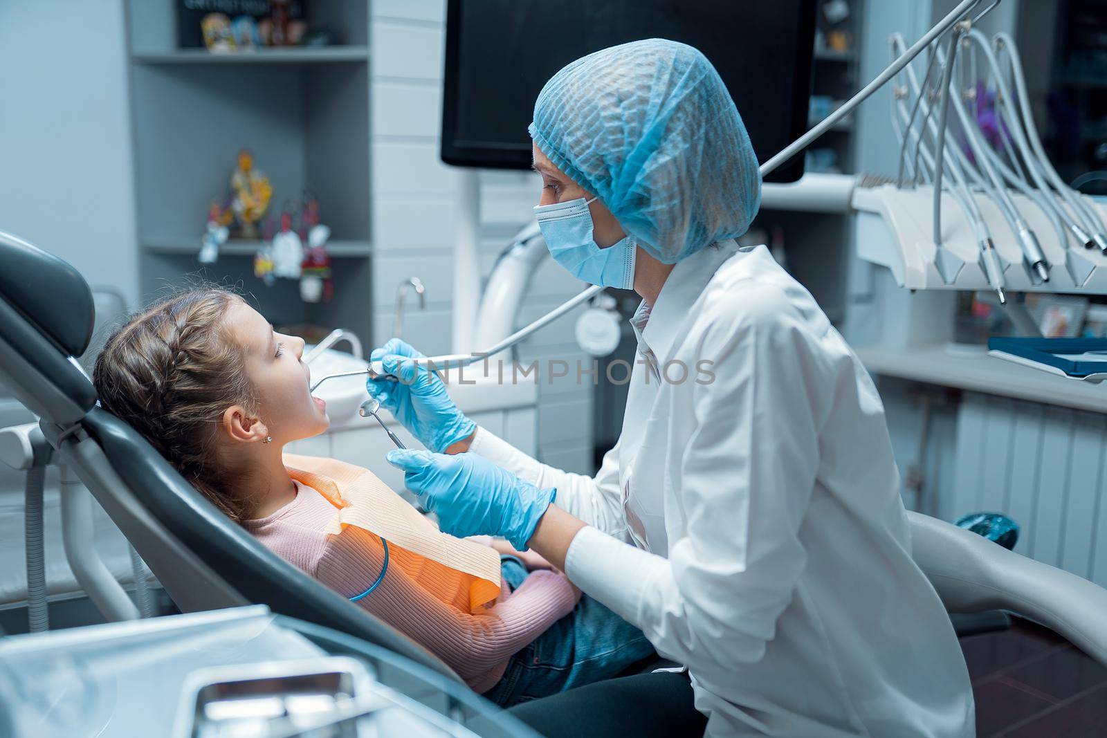 Female dentist stomatologist treats teeth of little girl patient at dental clinic. Dentistry concept