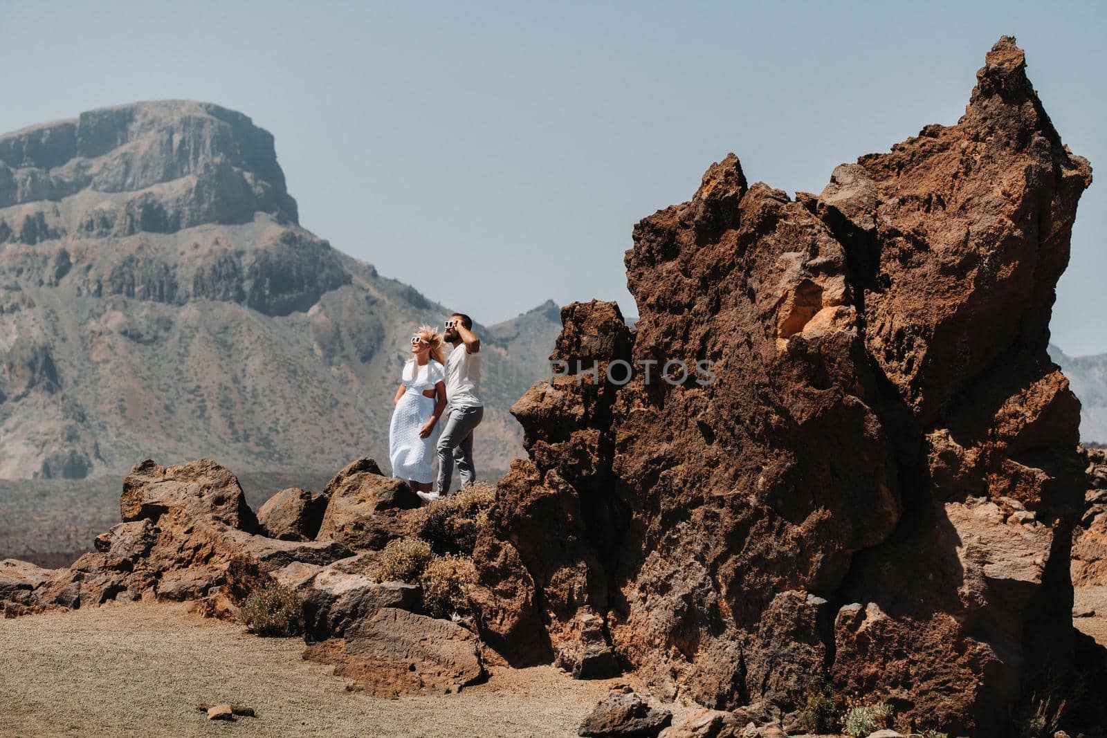 a guy and a girl in white clothes and glasses stand in the crater of the El Teide volcano, a Couple stands on a mountain in the crater of a volcano on the island of Tenerife, Spain.