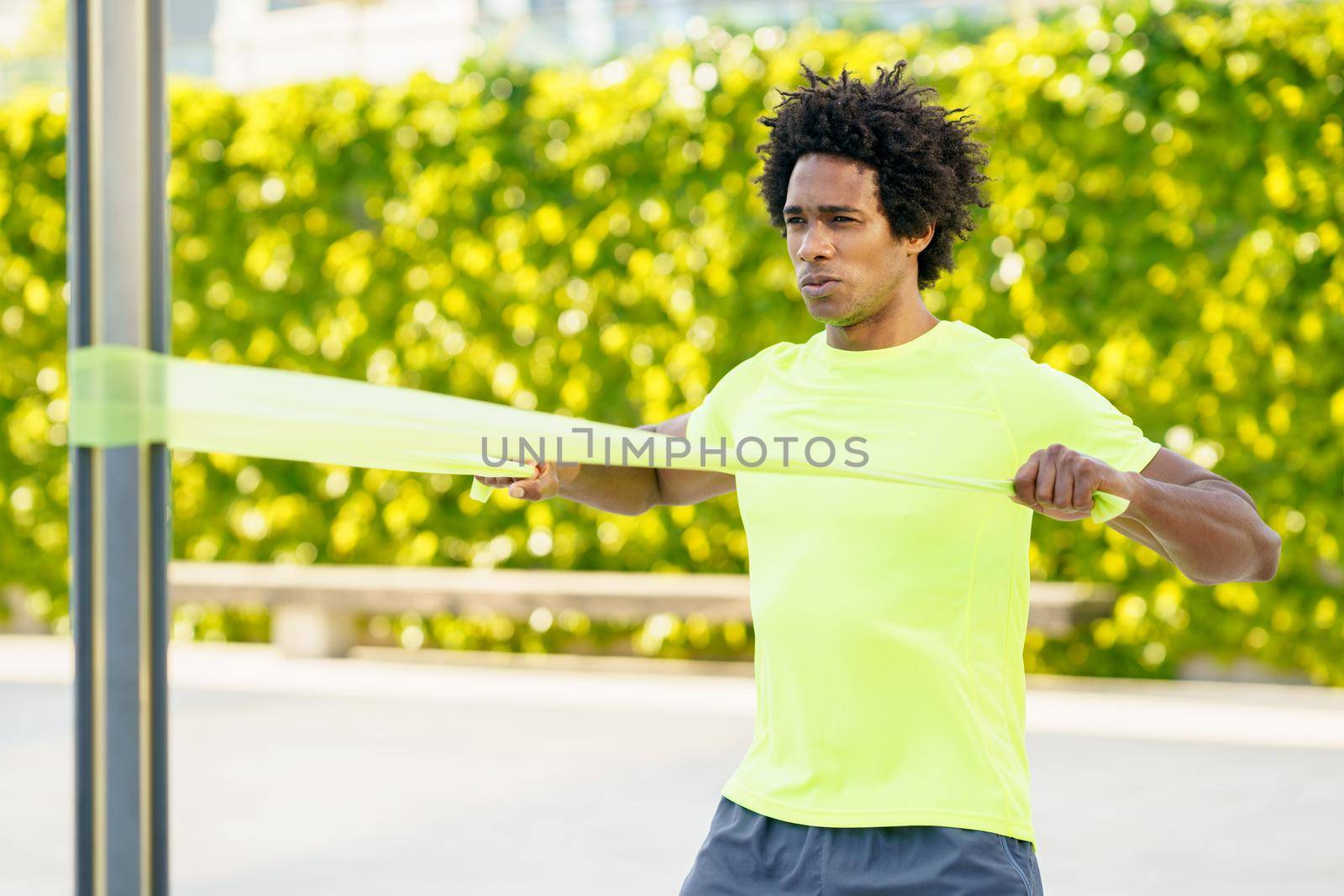 Black man working out with elastic band outdoors. Young male exercising in urban background.