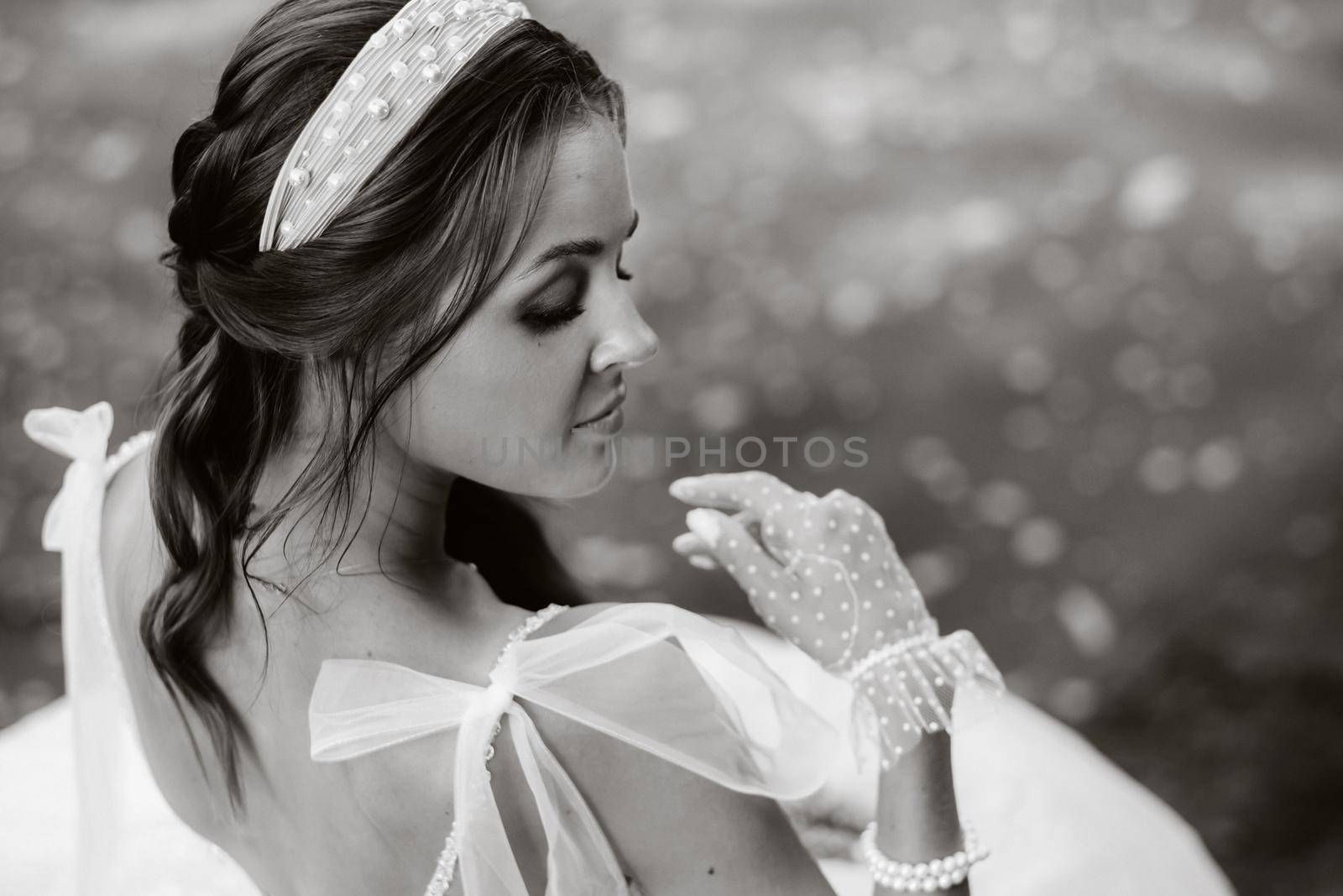 An elegant bride in a white dress, gloves and bare feet is sitting near a waterfall in the Park enjoying nature.A model in a wedding dress and gloves at a nature Park.Belarus. black and white photo by Lobachad