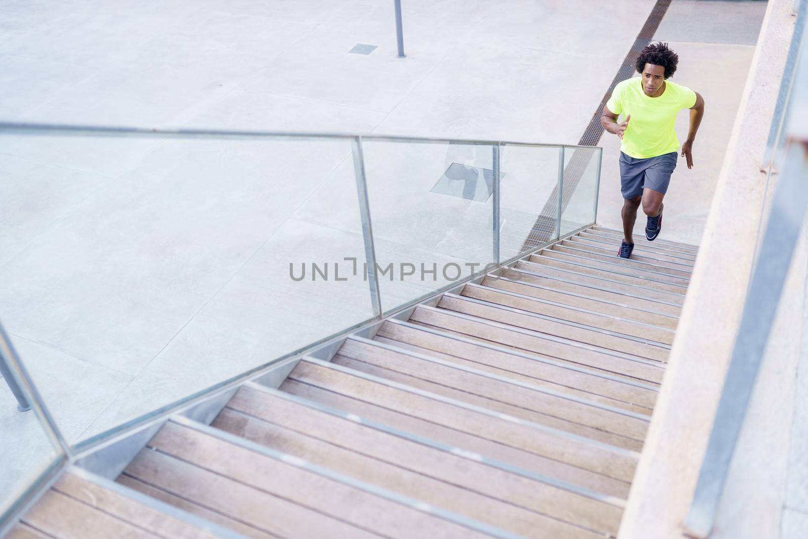 Black man running upstairs outdoors. Young male exercising in urban background.
