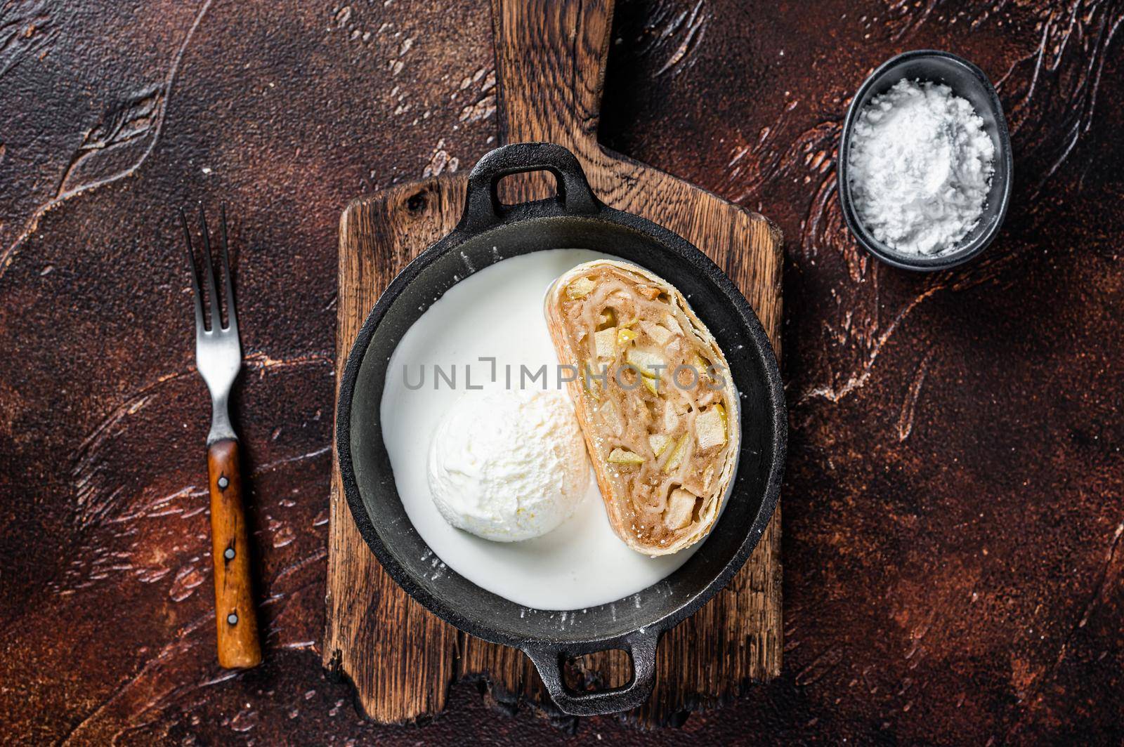 Apfelstrudel strudel with cinnamon, powdered sugar and vanilla ice cream in a pan. Dark background. Top view.