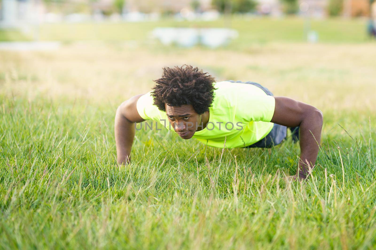 Black man doing push-ups exercising his chest on the grass of an urban park. Fitness, sport, exercising, training and people concept