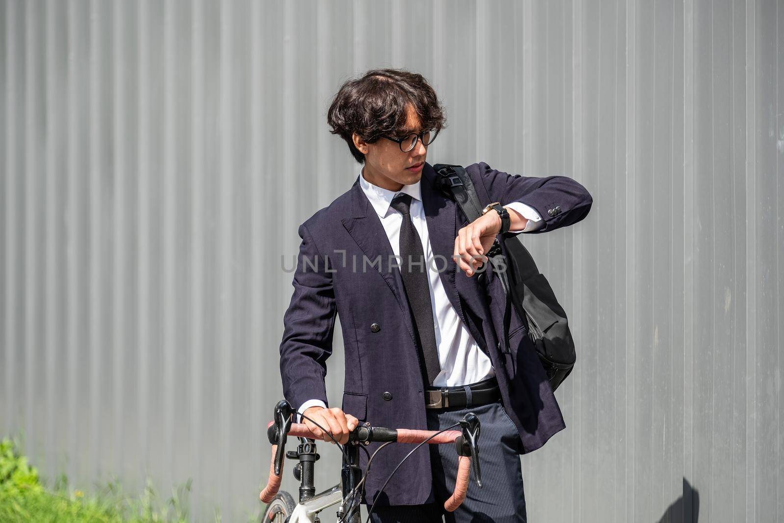 Asian businessman pushing his bicycle and looking on watch in the morning preparing to ride his bicycle to work. Eco tranportation.