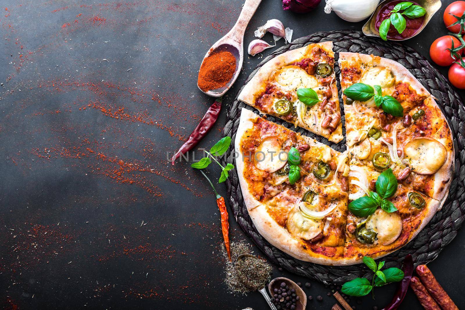 tasty pizza on a black background with spices and vegetables