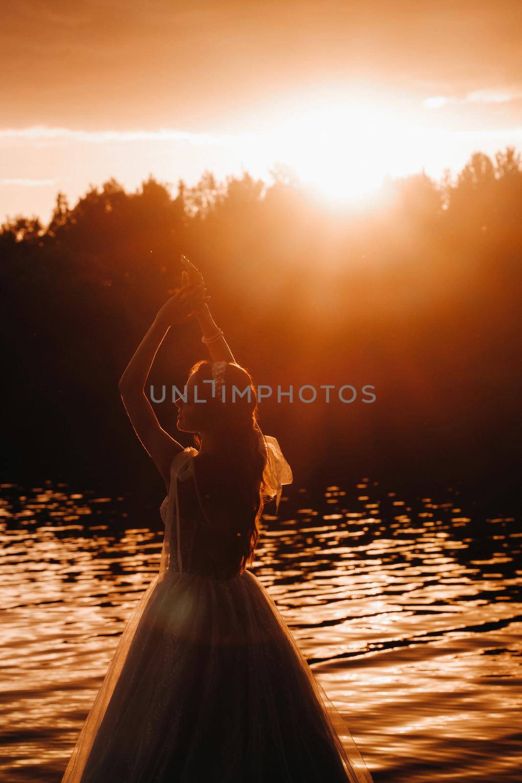 An elegant bride in a white dress enjoys nature at sunset.Model in a wedding dress in nature in the Park.Belarus by Lobachad