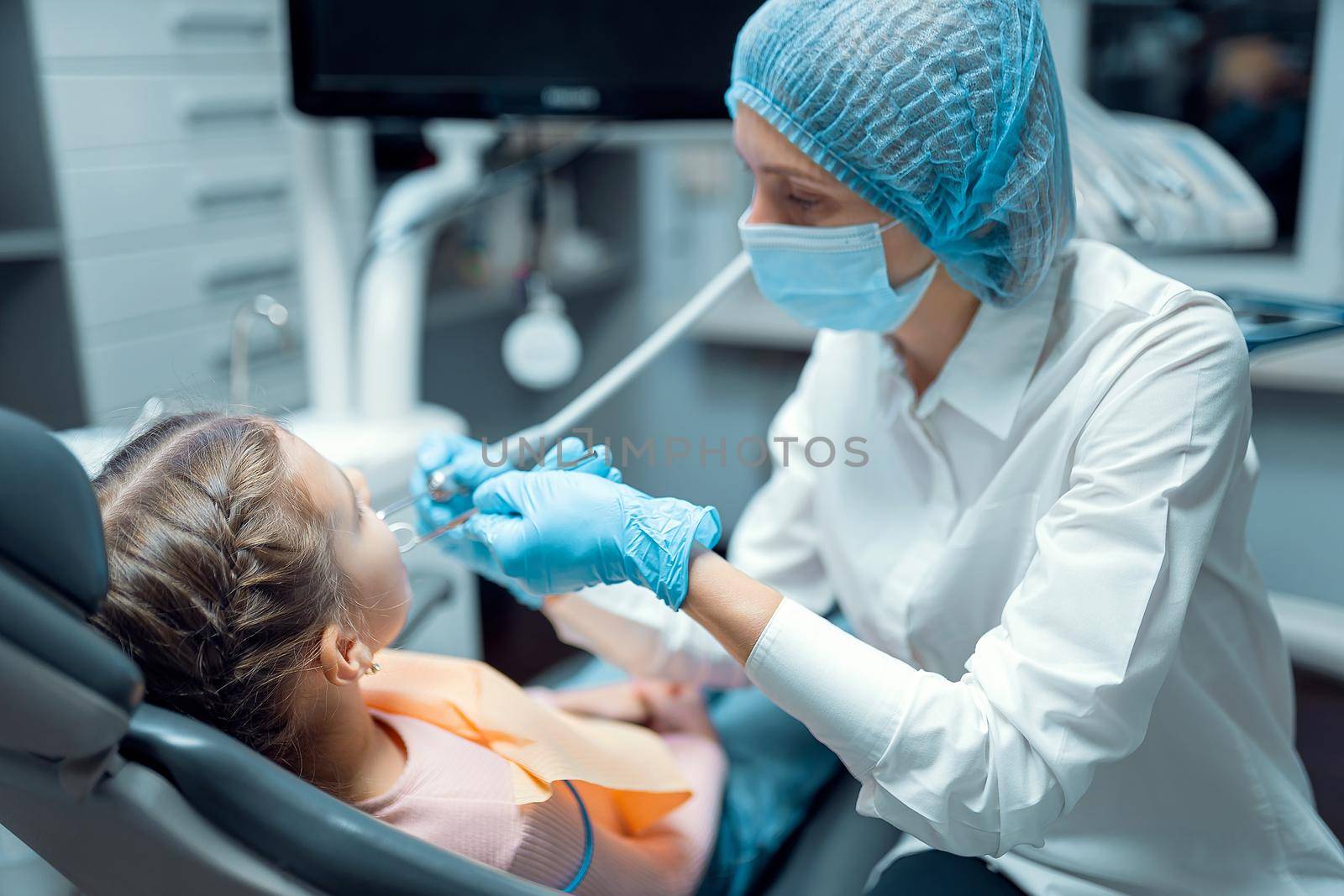 Female dentist stomatologist treats teeth of little girl patient at dental clinic. Dentistry concept .