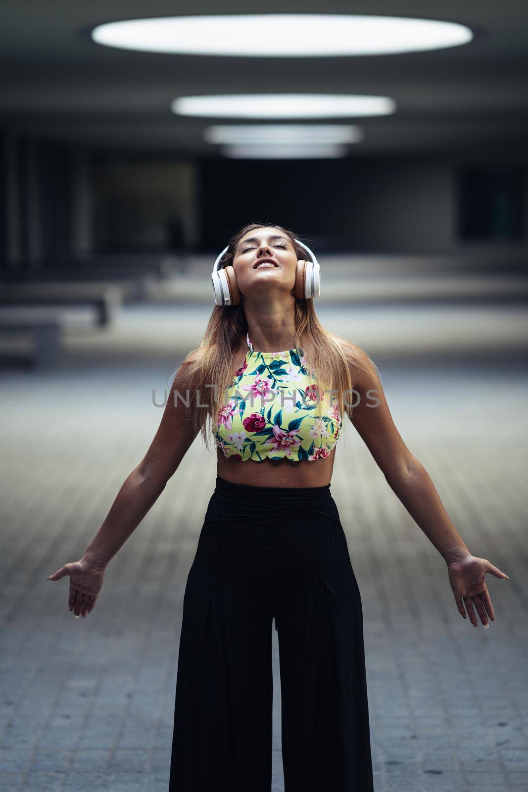 Young woman opening arms wearing headphones in urban background.