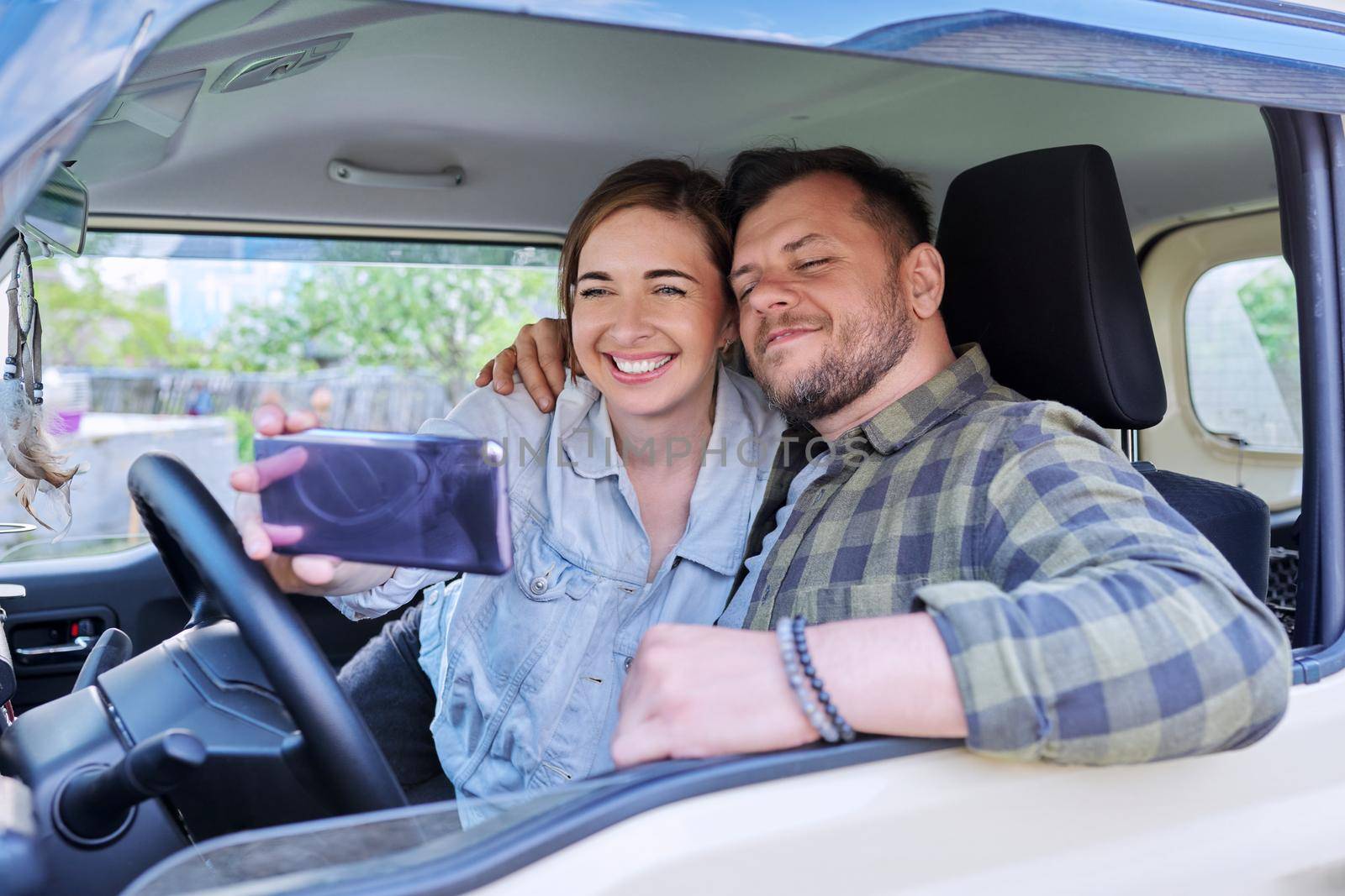 Happy married couple taking selfie photo on smartphone, husband and wife sitting in car.