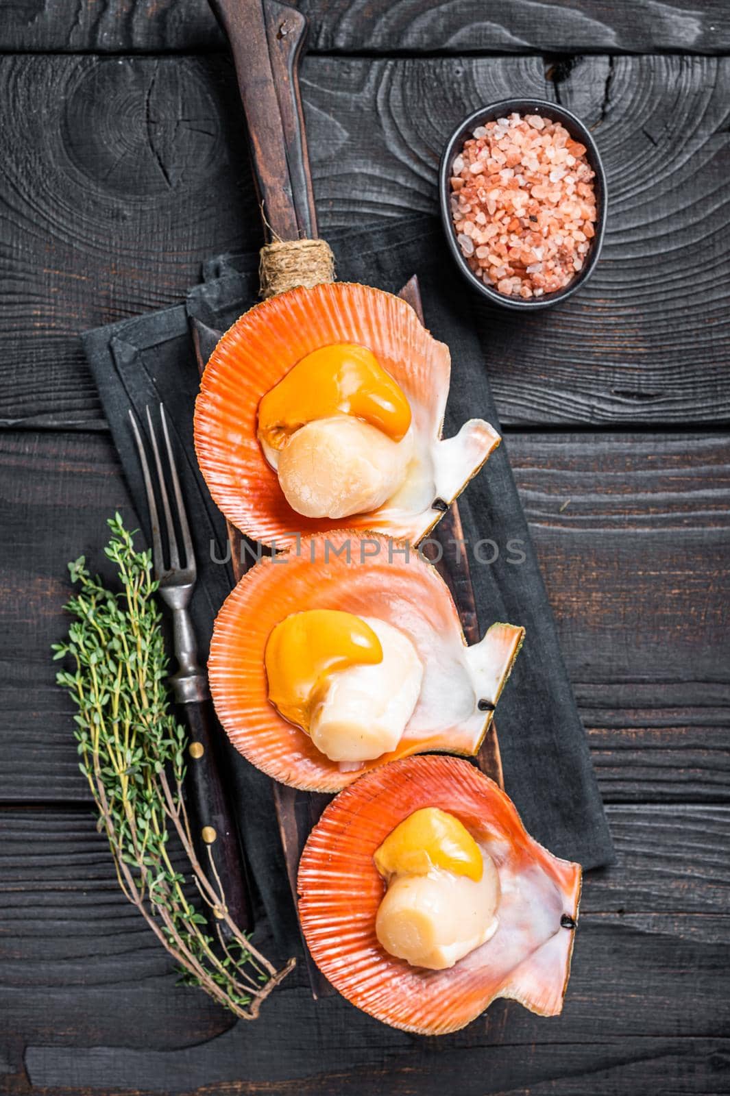 Scallops raw Shellfish on a wooden board with herbs. Black wooden background. Top view.