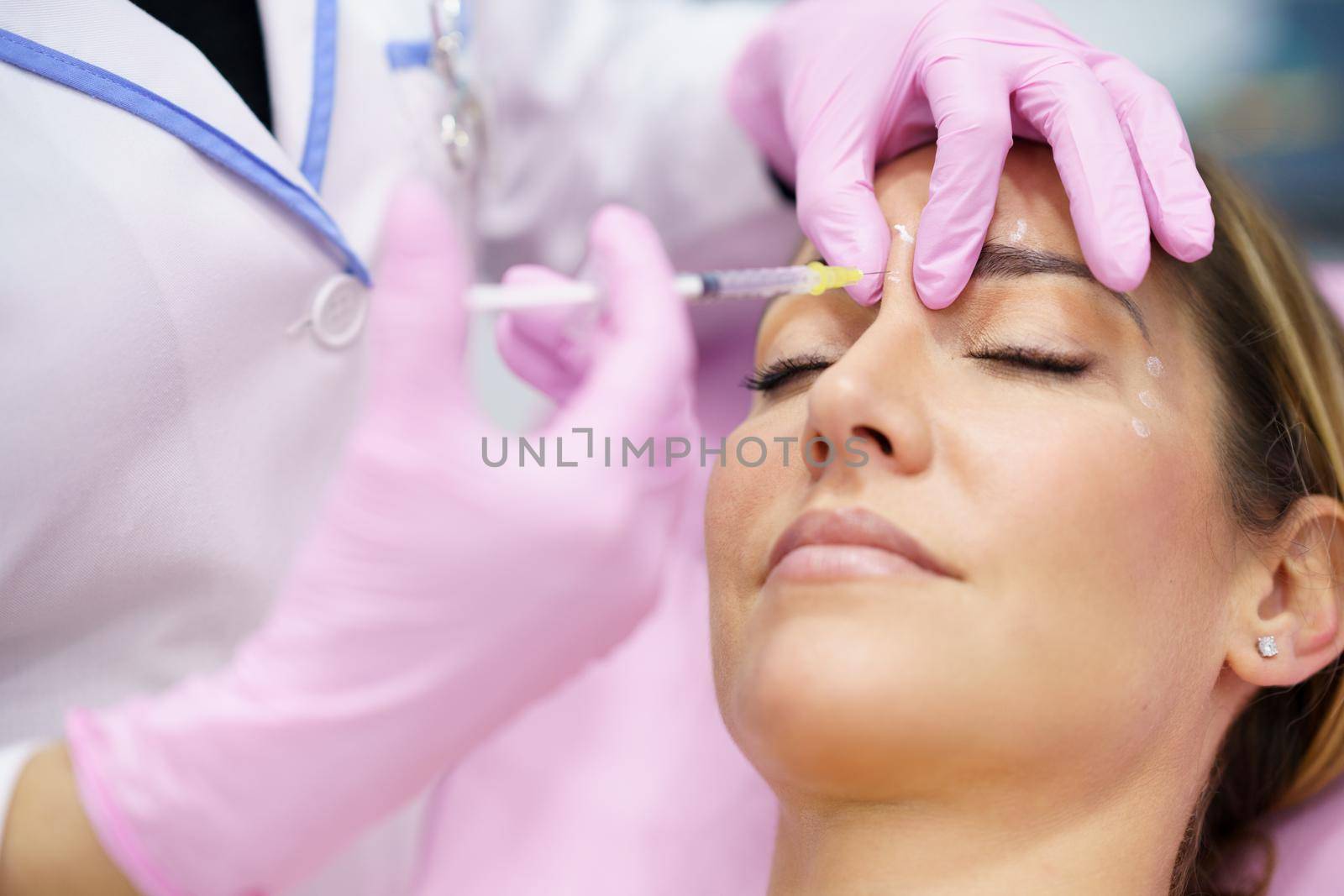 Aesthetic doctor injecting botulinum toxin into the forehead of her middle-aged patient. Facial treatment done in a cosmetic surgery clinic.