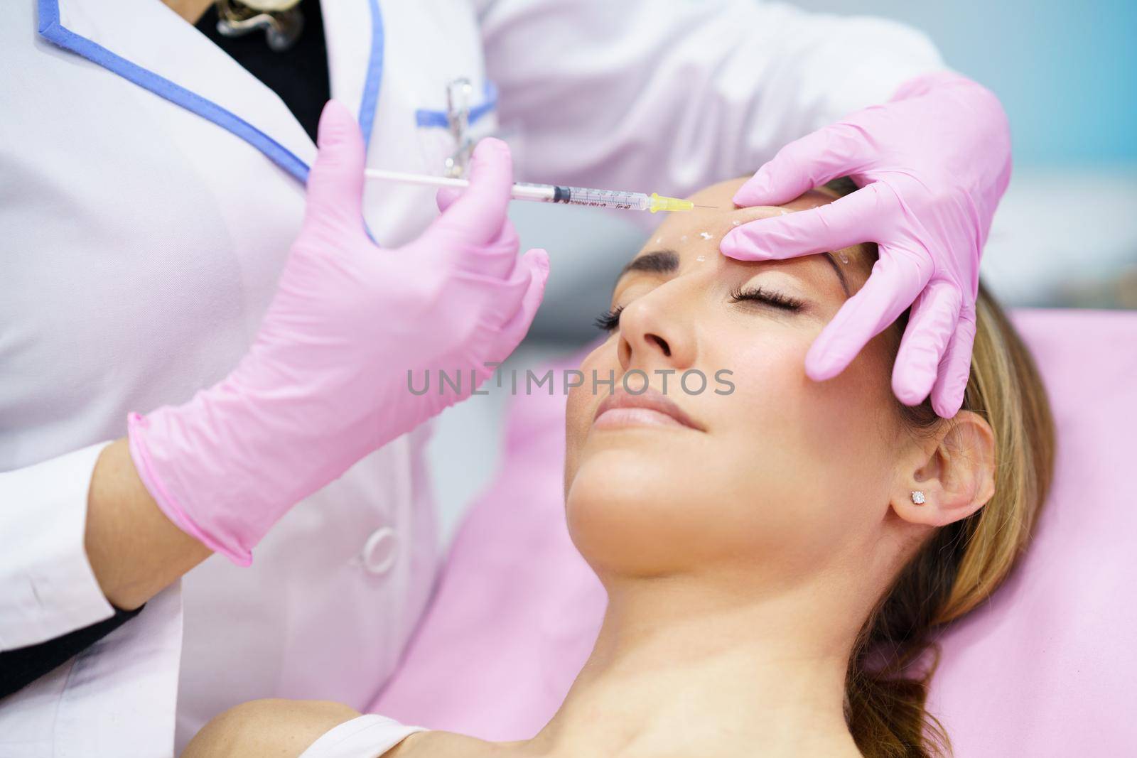 Aesthetic doctor injecting botox into the forehead of her middle-aged patient. Facial treatment done in a cosmetic surgery clinic.