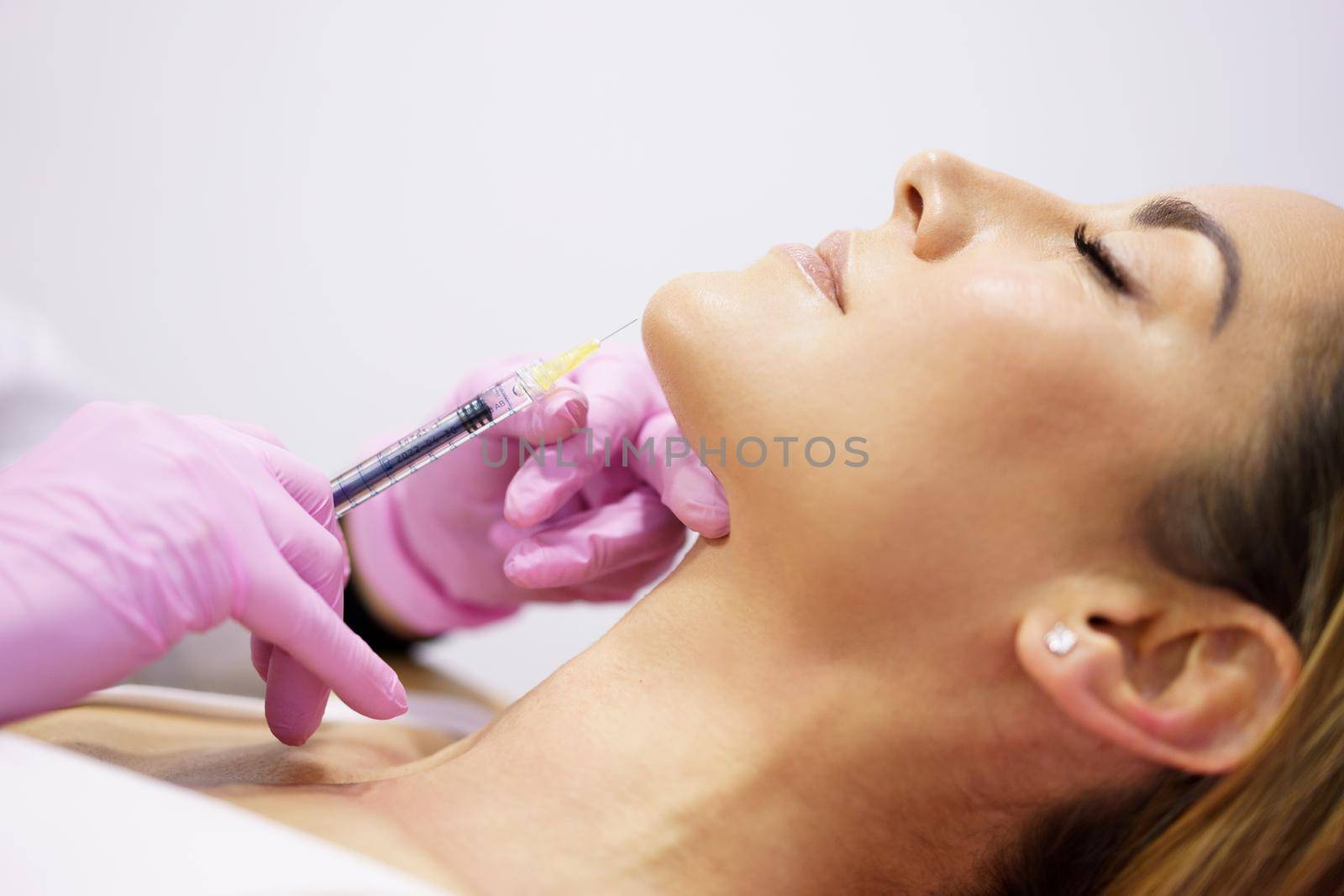 Doctor injecting hyaluronic acid into the chin of a middle-aged woman as a facial rejuvenation treatment.