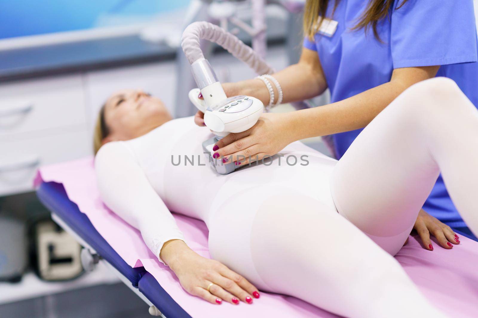 Middle-aged woman in special white suit having a anti cellulite belly massage with spa apparatus