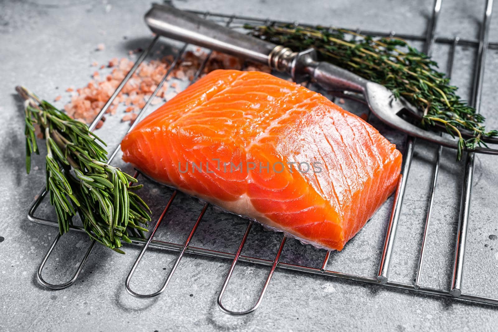 Cooking Raw salmon fillet steak on grill with herbs. Gray background. Top view.