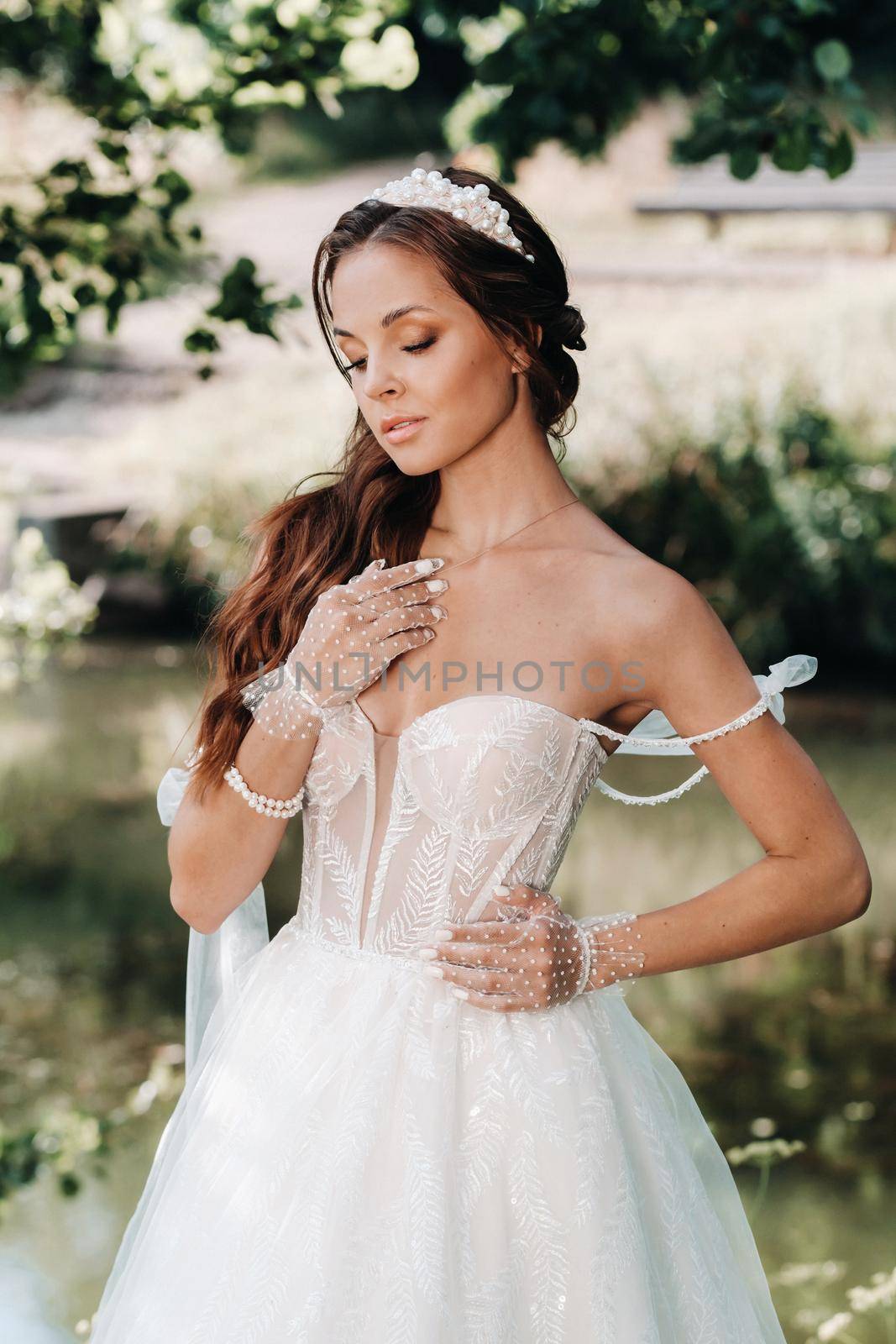 An elegant bride in a white dress, gloves with a bouquet on a waterfall in the Park, enjoying nature.Model in a wedding dress and gloves in the forest.Belarus.