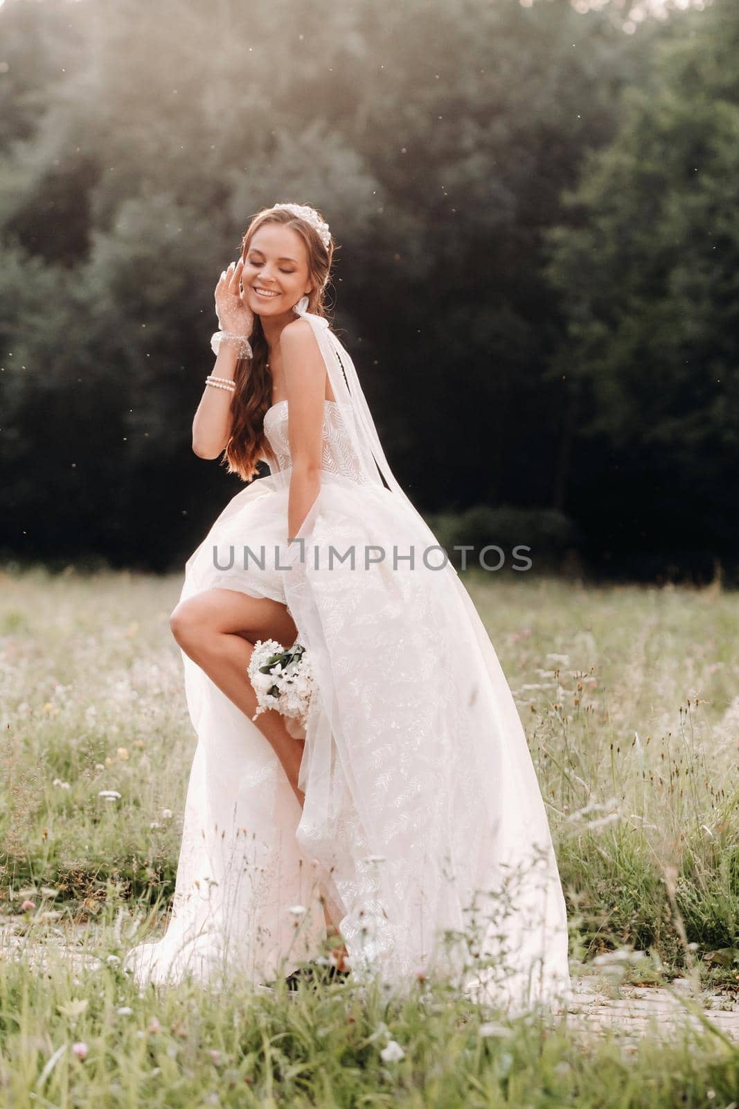 On the wedding day, an Elegant bride in a white long dress and gloves with a bouquet in her hands stands in a clearing enjoying nature. Belarus. by Lobachad