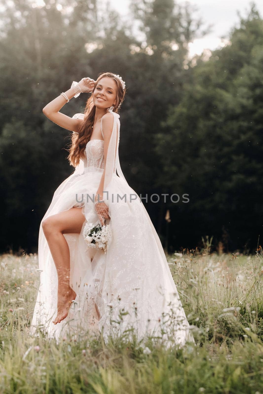 On the wedding day, an Elegant bride in a white long dress and gloves with a bouquet in her hands stands in a clearing enjoying nature. Belarus