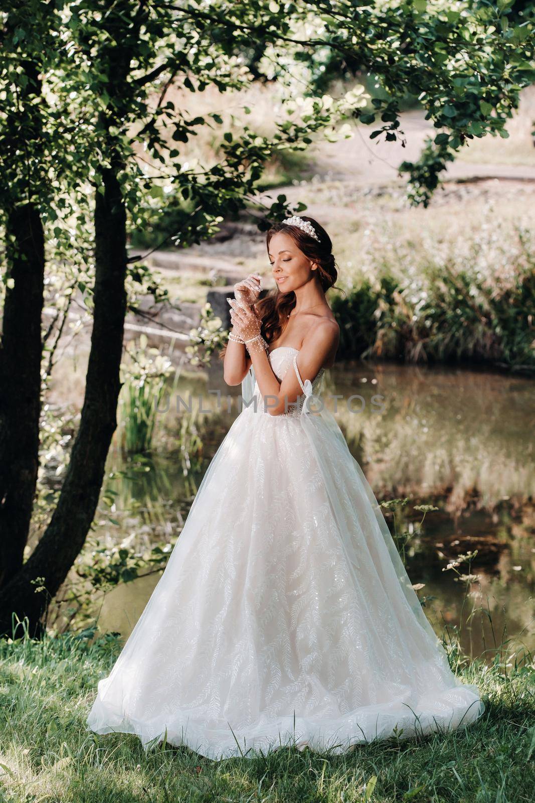 An elegant bride in a white dress, gloves with a bouquet on a waterfall in the Park, enjoying nature.Model in a wedding dress and gloves in the forest.Belarus.